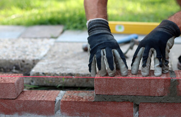 Construction work in progress. Male builder working with red bricks. Masonry wall close up photo.  