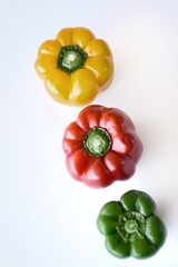 Tres pimientos de color rojo, amarillo y verde sobre fondo blanco.
