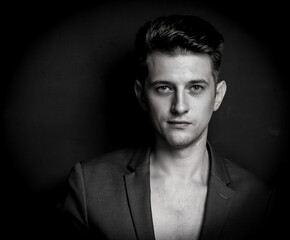 Monochrome portrait of young man. Black and white photo of male in black jacket on dark backdrop.