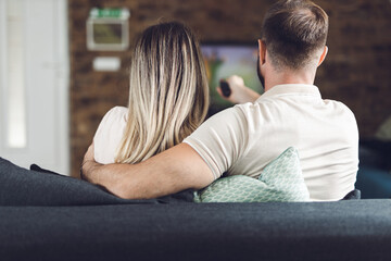 Back view of a couple sitting on sofa and watching a TV at home
