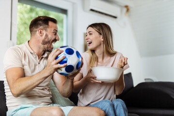 Cheerful couple celebrating the victory of their soccer team at home