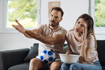 Displeased young couple watching a soccer match at home