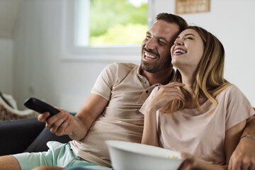 Cheerful young couple laughing while watching television at home