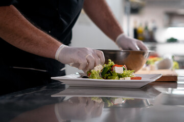 Obraz na płótnie Canvas chef cook hands in gloves prepare or put healthy greek salad on plate at kitchen