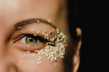 Open, green eye of a woman with white sesame seeds on the eyelid, around the eye. Expressive look.