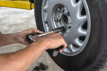 An asian mechanic loosens and removes the lug nuts from the tire of a serviced car with a ratchet...