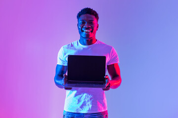 Check this website. Handsome young black man holding laptop with blank screen in neon light, mockup...