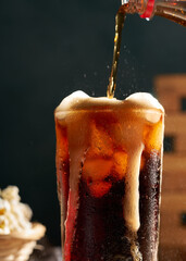 pouring cola soda into glass on wooden table with popcorn
