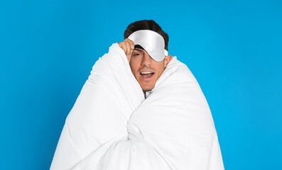 Man wrapped in blanket wearing sleeping mask on blue background