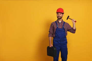 Professional builder in uniform with hammer and toolbox on yellow background, space for text