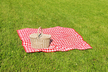 Picnic basket with checkered tablecloth on green grass outdoors