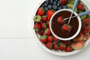 Fondue pot with chocolate and mix of fruits on white wooden table, top view. Space for text