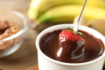 Dipping strawberry into fondue pot with chocolate, closeup