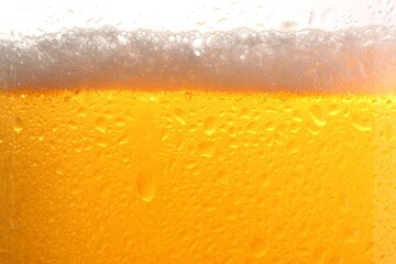 Glass of tasty cold beer with foam and condensation drops on white background, closeup