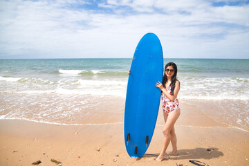 South American woman, young and beautiful, brunette with sunglasses and swimsuit and holding a blue surfboard. Concept sea, sand, sun, beach, vacation, surf, summer.