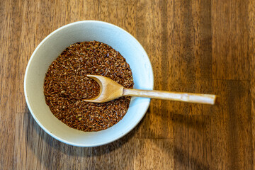 Selective focus on linseed or flax seed and a spoon in a white bowl on wooden background. Top view. Healthy food concept. Copy for text. Noise effect and grainy texture. 