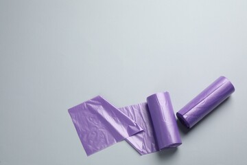 Rolls of violet garbage bags on light grey background, flat lay. Space for text