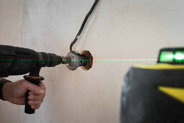 Electrical wiring work using laser level device. Man drilling round holes on the wall for sockets...