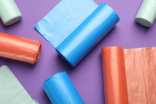 Rolls of different color garbage bags on violet background, flat lay