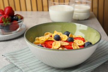 Corn flakes with berries in bowl served on grey table, closeup