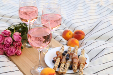 Glasses of delicious rose wine, flowers and food on white picnic blanket