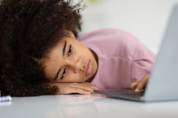 Closeup of bored black girl lying on desk with laptop