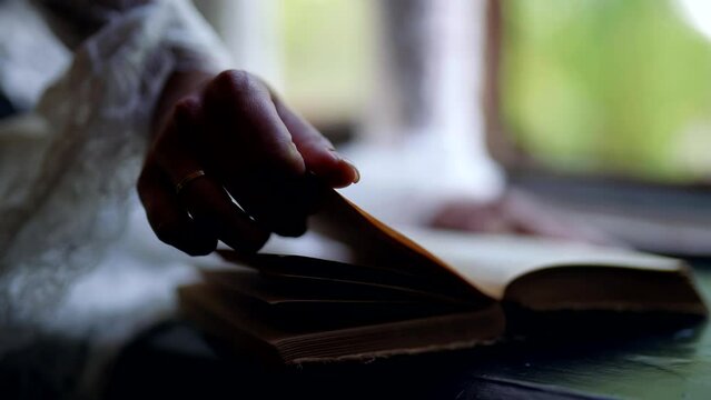 woman is reading old book, closeup view of female hands flipping pages, romantic vintage shot