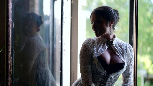 seductive lady with big breasts in vintage dress is resting in village house, sitting on window