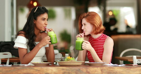 Multicultural friends toasting with green juice. Multiracial young women drinking healthy veggie...