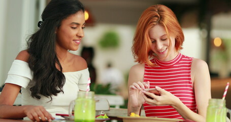 Girl showing friend cellphone screen laughing and smiling, multiracial friendship