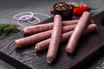 Raw sausages with spices on a wooden cutting board on a stone background with copy space for your text