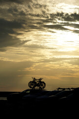 Silhouettes of bicycles on a car in front of a dramatic cloudy sky