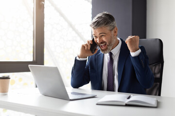 Joyful Middle Aged Businessman With Cellphone And Laptop Celebrating Success In Office