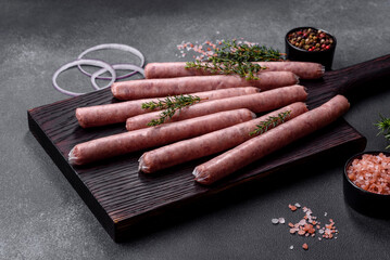 Raw sausages with spices on a wooden cutting board on a stone background with copy space for your text