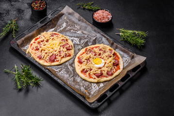 Homemade pizza with sausages, tomatoes, cheese, spices and herbs on a wooden cutting board