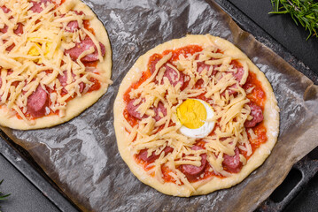 Homemade pizza with sausages, tomatoes, cheese, spices and herbs on a wooden cutting board