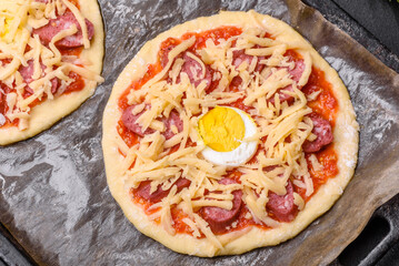Homemade pizza with sausages, tomatoes, cheese, spices and herbs on a wooden cutting board