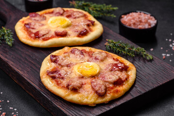Homemade pizza with sausages, tomatoes, cheese, spices and herbs on a wooden cutting board