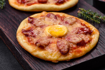 Homemade pizza with sausages, tomatoes, cheese, spices and herbs on a wooden cutting board