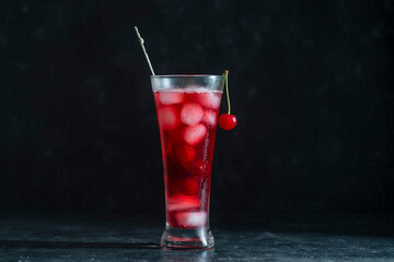 Fresh red cherry cocktail with ice cubes in glass on black background. Summer iced refreshing drink