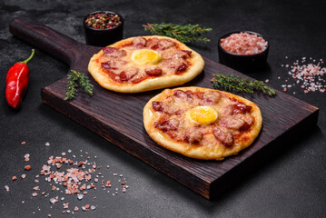 Homemade pizza with sausages, tomatoes, cheese, spices and herbs on a wooden cutting board