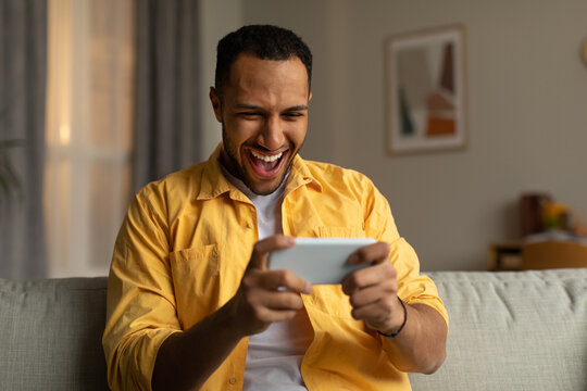 Overjoyed Young Black Man With Smartphone Feeling Excited Over Winning Lottery Or Casino Bet Online At Home