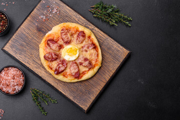 Homemade pizza with sausages, tomatoes, cheese, spices and herbs on a wooden cutting board