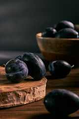 Delicious ripe blue plums in bowl on black table, closeup