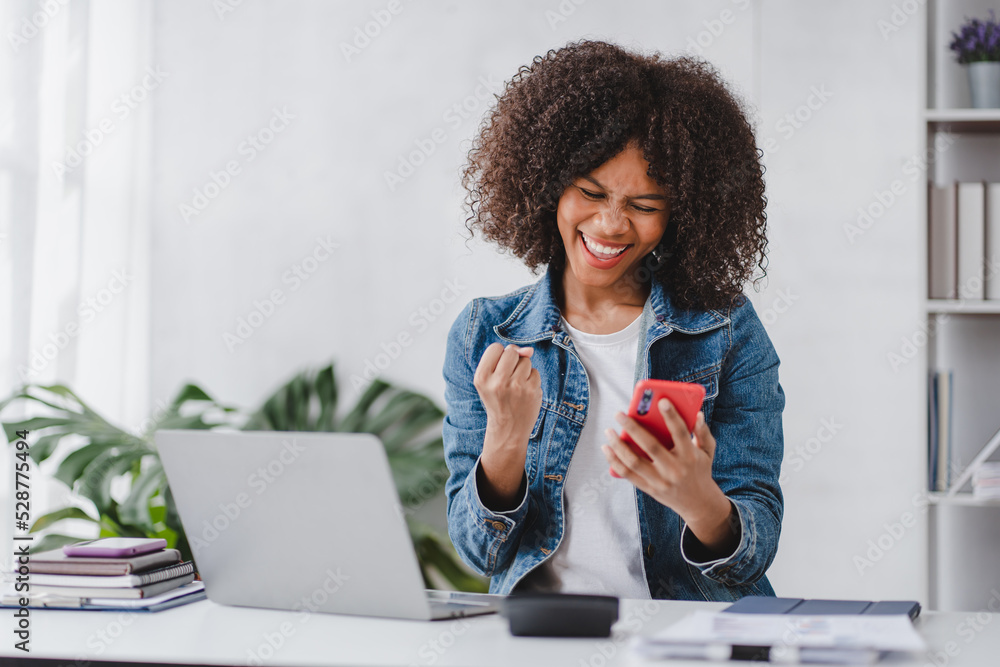 Wall mural successful and exciting african american businesswoman Young woman excited to win on her smartphone at work.