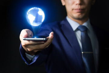 Asian business person using smartphone with 3D illusion digital global, icons and globe with dark black background Global business concept, 3D Rendering.