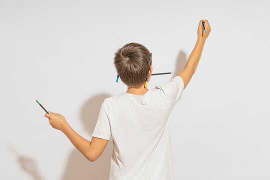 A teenager draws on the wall, standing with his back to the camera. Hard light, white background.