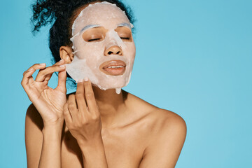 African American woman applies cosmetic tissue facial mask for hydrating and moisturizing and...