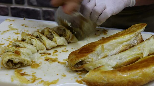 The cook is cutting the cooked mince pastry. Turkish food mince pastry dish: " kol boregi "