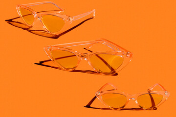sunglasses with yellow lenses in a transparent frame on an orange background with hard light